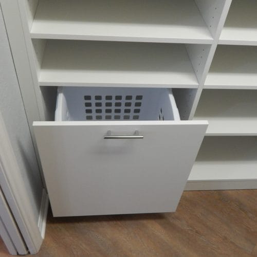 Custom walk-in closet design by Gulfshore Closets in Naples, Florida, featuring built-in laundry hamper, drawers, and shoe shelves for organizing a large clothing collection.