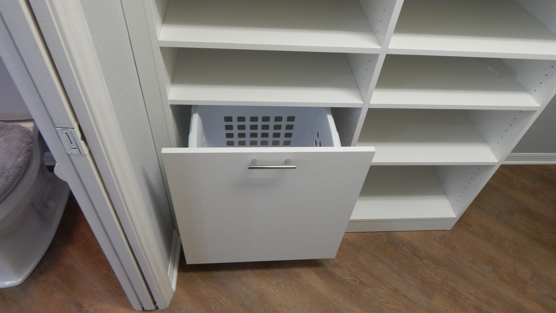 Custom walk-in closet design by Gulfshore Closets in Naples, Florida, featuring built-in laundry hamper, drawers, and shoe shelves for organizing a large clothing collection.